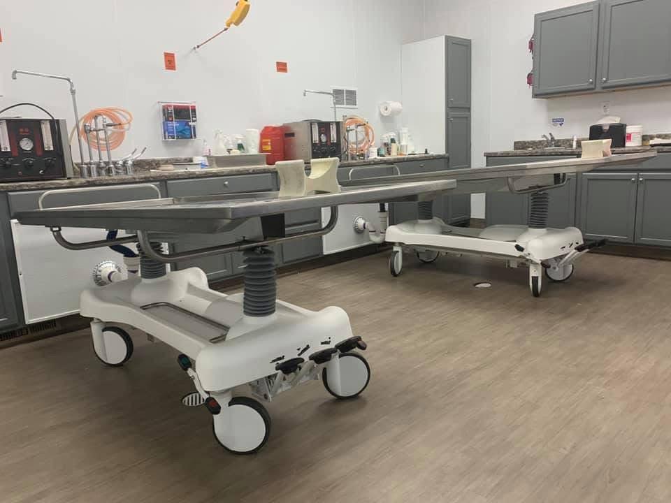 A side-by-side view of a hydraulic embalming table and a folded dressing table, emphasizing space-saving design